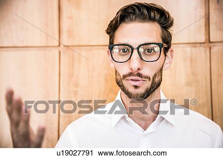 Stock Image - Young man wearing glasses looking at camera smiling, gesticulating. Fotosearch