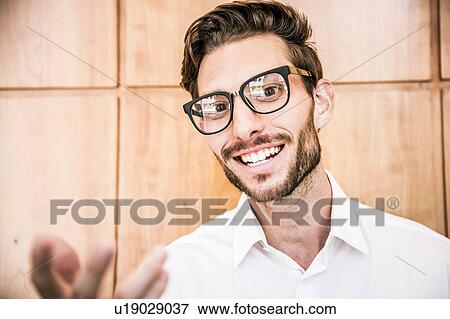 Stock Photo - Young man wearing glasses looking at camera smiling, gesticulating. Fotosearch