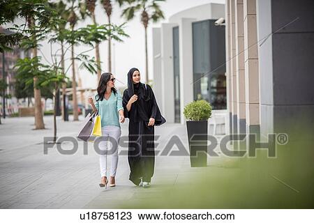 Young middle eastern woman wearing traditional clothing walking along street with female friend, Dubai, United Arab Emirates View Large Photo Image Stock Image - Young middle eastern woman wearing traditional clothing walking along street with female friend, Dubai, United Arab Emirates. Fotosearch