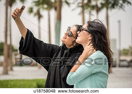 Young middle eastern woman wearing traditional clothing taking smartphone selfie with female friend, Dubai, United Arab Emirates View Large Photo Image Stock Photo - Young middle eastern woman wearing traditional clothing taking smartphone selfie with female friend, Dubai, United Arab Emirates. Fotosearch