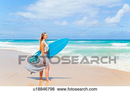 Stock Photo - Young woman carrying surfboard on beach, Dominican Republic, The Caribbean. Fotosearch
