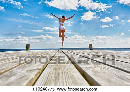 Young woman dancing on wooden pier, mid air, rear view View Large Photo Image Stock Photography - Young woman dancing on wooden pier, mid air, rear view. Fotosearch
