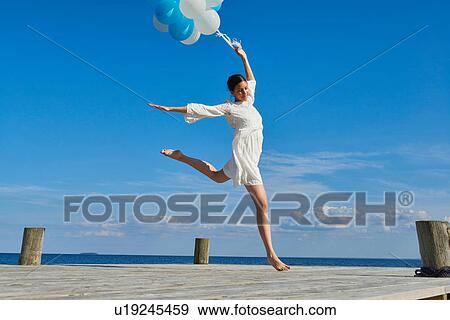 Young woman dancing on wooden pier, holding bunch of balloons View Large Photo Image Stock Photo - Young woman dancing on wooden pier, holding bunch of balloons. Fotosearch