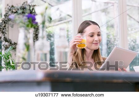 Stock Photo - Young woman holding glass of orange juice using digital tablet. Fotosearch