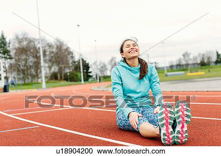 Stock Image - Young woman on running track, exercising, stretching. Fotosearch
