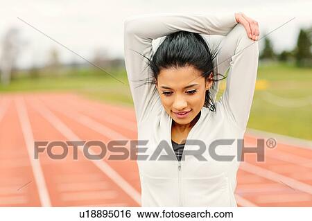 Stock Photograph - Young woman on running track, exercising, stretching. Fotosearch