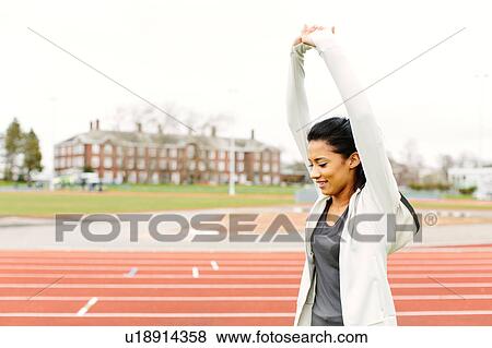 Stock Photo - Young woman on running track, stretching. Fotosearch
