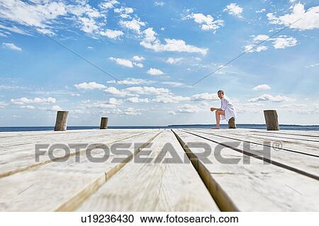 Young woman sitting on post on wooden pier, relaxing View Large Photo Image Stock Image - Young woman sitting on post on wooden pier, relaxing. Fotosearch