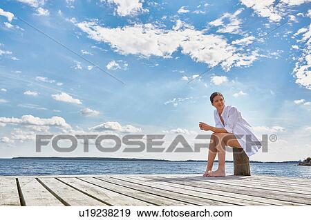 Young woman sitting on post on wooden pier, looking away View Large Photo Image Stock Photo - Young woman sitting on post on wooden pier, looking away. Fotosearch