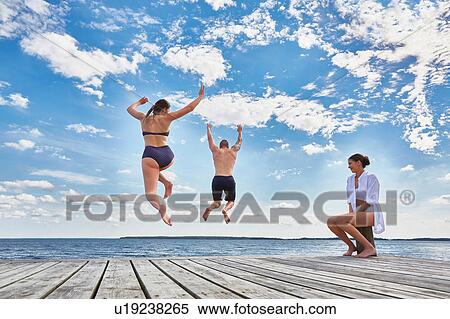 Young woman sitting on post on wooden pier, watching friends jump into sea, rear view View Large Photo Image Stock Photography - Young woman sitting on post on wooden pier, watching friends jump into sea, rear view. Fotosearch