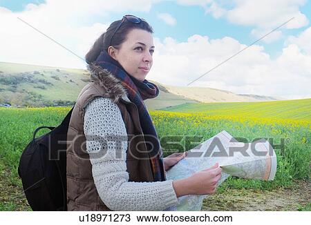 Stock Image - Young woman standing in field, holding map. Fotosearch