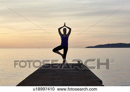 Young woman standing on pier, in yoga position, at sunset View Large Photo Image Stock Image - Young woman standing on pier, in yoga position, at sunset. Fotosearch
