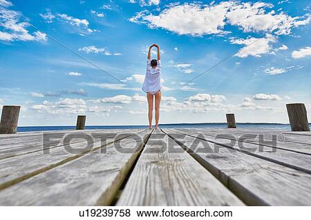 Young woman standing on wooden pier, stretching, rear view View Large Photo Image Stock Photo - Young woman standing on wooden pier, stretching, rear view. Fotosearch