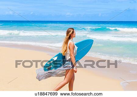 Stock Photo - Young woman strolling on beach carrying surfboard, Dominican Republic, The Caribbean. Fotosearch