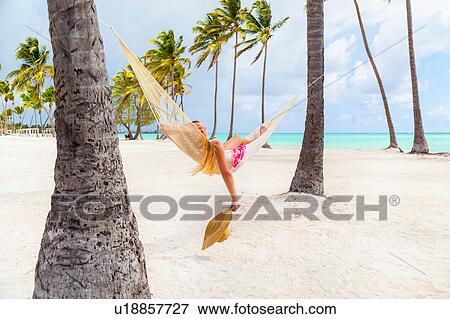 Stock Photo - Young woman sunbathing in palm tree hammock at beach, Dominican Republic, The Caribbean. Fotosearch