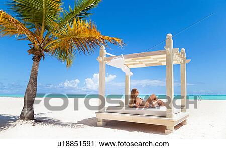 Stock Image - Young woman wearing bikini sunbathing on beach daybed, Dominican Republic, The Caribbean. Fotosearch