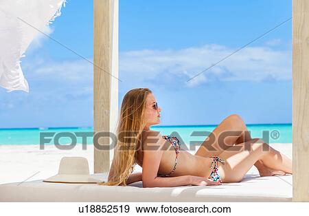 Stock Photo - Young woman wearing bikini sunbathing on beach daybed, Dominican Republic, The Caribbean. Fotosearch