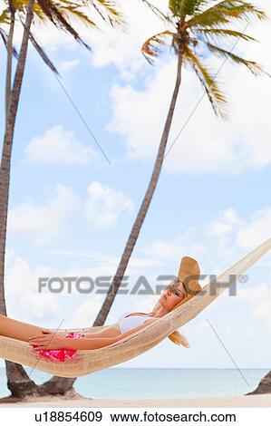 Stock Photo - Young woman wearing bikini sunbathing in beach hammock, Dominican Republic, The Caribbean. Fotosearch