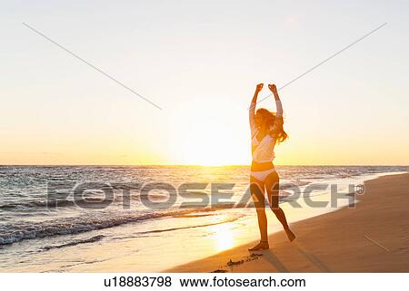 Stock Photo - Young woman with arms raised on beach at sunset, Dominican Republic, The Caribbean. Fotosearch