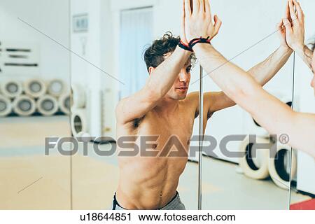 Stock Image - Bare chested man leaning against mirror looking at himself. Fotosearch