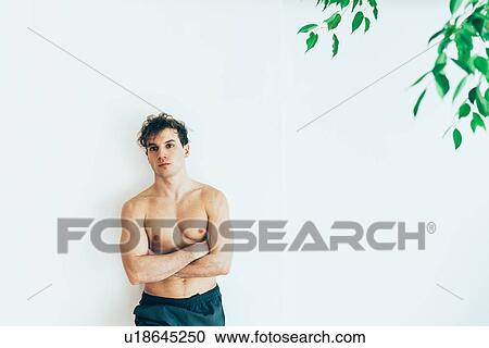 Stock Image - Bare chested man leaning against wall, arms crossed looking at camera. Fotosearch