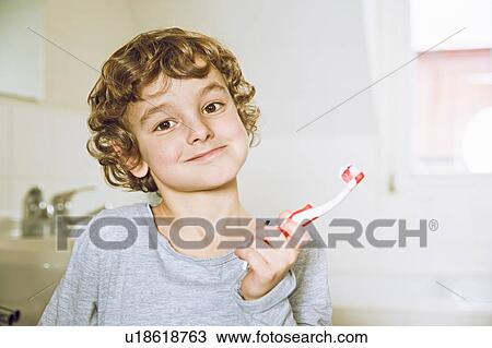 Stock Image - Boy in bathroom holding toothbrush looking at camera smiling. Fotosearch