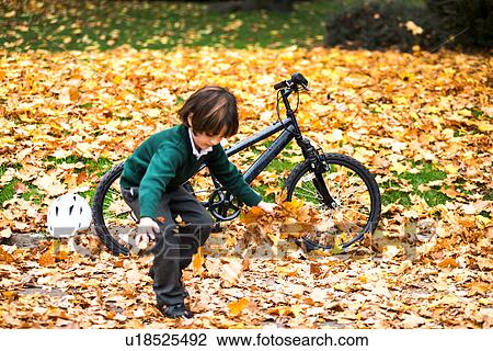Stock Image - Boy in park with bike playing in autumn leaves. Fotosearch