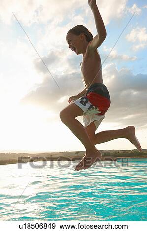 Stock Photo - Boy jumping mid air into swimming pool, Buonconvento, Tuscany, Italy. Fotosearch