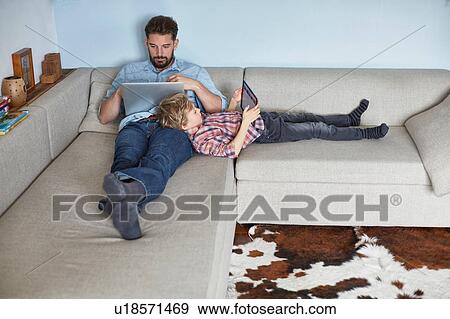 Stock Photo - Boy lying on sofa with father using technology. Fotosearch