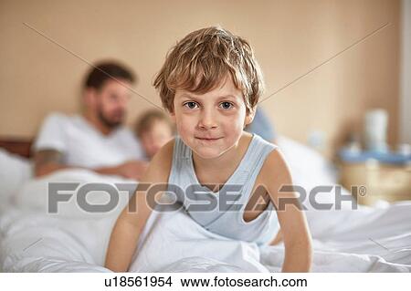 Picture - Boy on parents bed looking at camera smiling. Fotosearch
