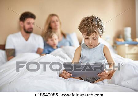 Stock Photography - Boy on parents bed using digital tablet. Fotosearch