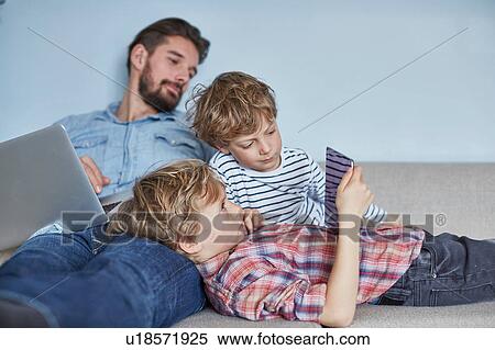 Boys lying on sofa with father using technology View Large Photo Image Stock Photography - Boys lying on sofa with father using technology. Fotosearch
