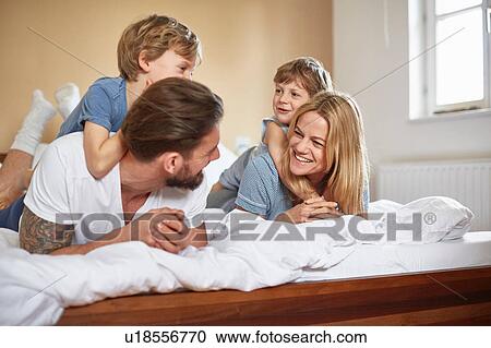 Boys on bed lying on top of parents face to face smiling View Large Photo Image Stock Image - Boys on bed lying on top of parents face to face smiling. Fotosearch