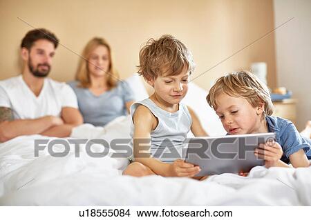 Boys on parents bed using digital tablet View Large Photo Image Picture - Boys on parents bed using digital tablet. Fotosearch