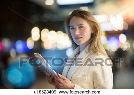 Stock Photo - Businesswoman using digital tablet on city street at night. Fotosearch