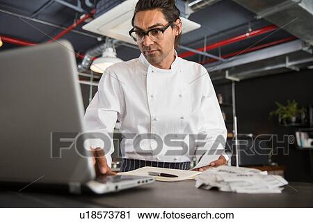 Stock Image - Chef in restaurant using laptop. Fotosearch