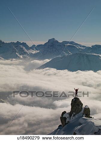 Stock Photo - Climber celebrating on peak emerging from fog, Bettmeralp, Valais, Switzerland. Fotosearch