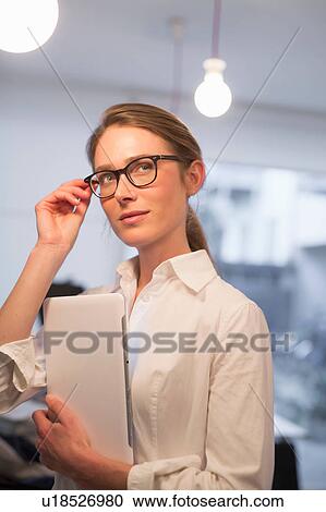 Stock Image - Confident businesswoman looking sideways whilst using digital tablet in office. Fotosearch