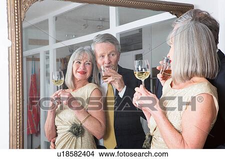 Picture - Couple dressed up and having drink in front of mirror. Fotosearch
