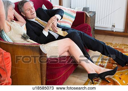 Stock Image - Couple dressed up, sitting on sofa and checking the time. Fotosearch