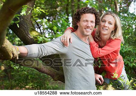Stock Photo - Couple leaning against tree looking at camera smiling. Fotosearch