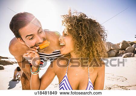 Stock Photo - Couple sharing ice lolly on beach, Cape Town, South Africa. Fotosearch