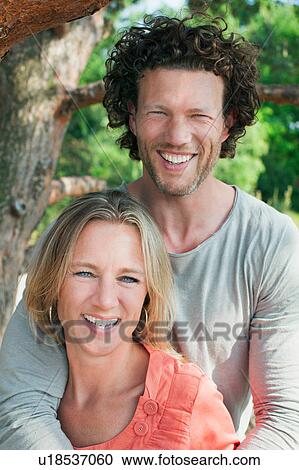Couple standing by tree looking at camera smiling View Large Photo Image Stock Image - Couple standing by tree looking at camera smiling. Fotosearch