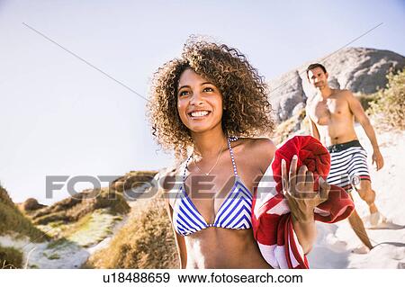 Stock Photo - Couple walking down sand dune carrying beach towel, Cape Town, South Africa. Fotosearch