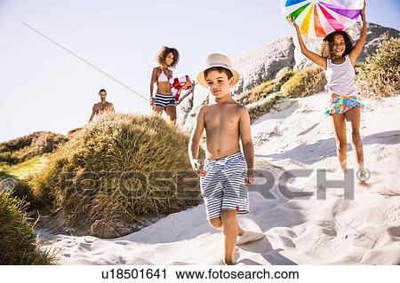 Stock Image - Family and two children walking down sand dune carrying beachball, Cape Town, South Africa. Fotosearch