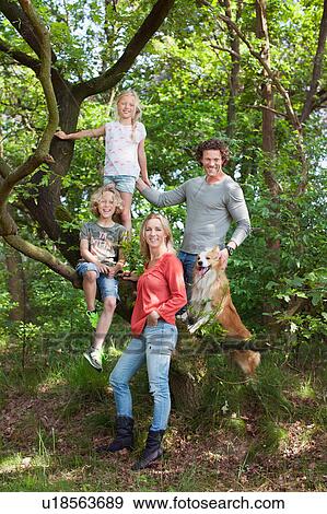 Stock Photo - Family in forest climbing tree looking at camera smiling. Fotosearch