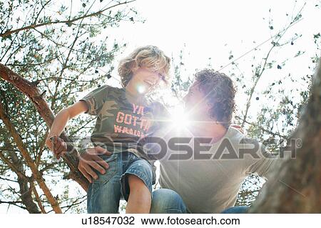 Stock Image - Father and son climbing tree. Fotosearch