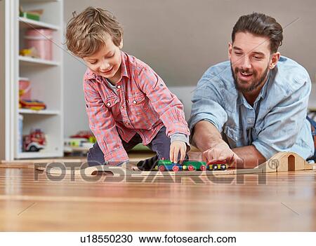 Stock Image - Father and son playing with wooden toy train set. Fotosearch