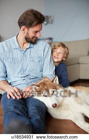 Stock Image - Father and son sitting with dog face to face smiling. Fotosearch