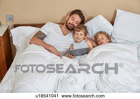 Father and sons in bed using digital tablet View Large Photo Image Stock Image - Father and sons in bed using digital tablet. Fotosearch